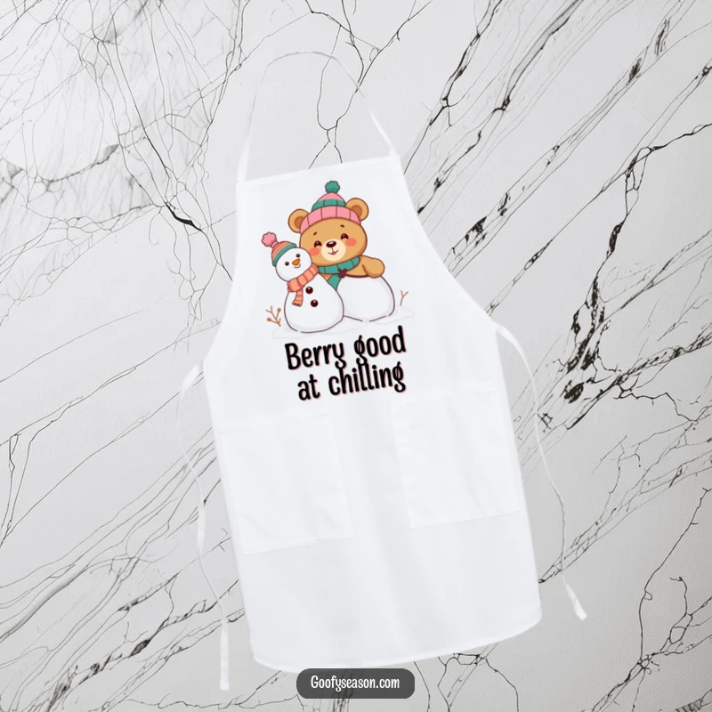 Funny apron depicting a curious bear character building a snowman, wearing a collection of mismatched, humorous hats while cooking.