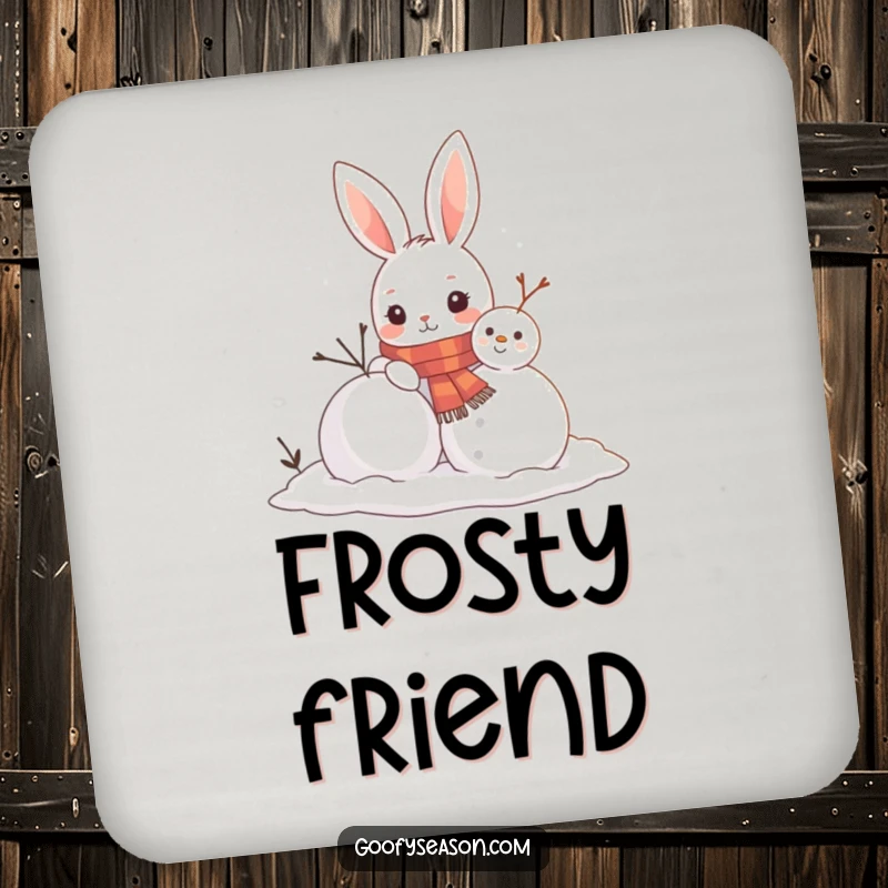 Funny drink coaster showing a curious bunny wearing a scarf building a snowman, adding a cheerful winter touch to any table.