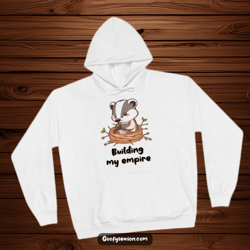 Funny hoodie featuring a clever badger character building a snug nest with twigs, embodying a humorous and comforting scene of home creation.