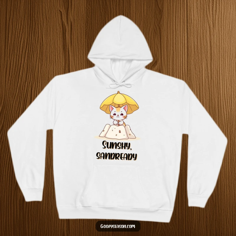 Funny, cozy hoodie depicting a curious cat holding a sun umbrella near a sandcastle on a sunny beach.