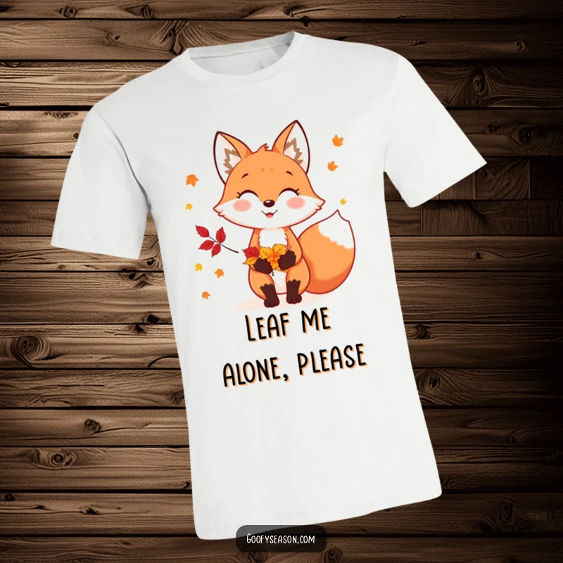 Funny t-shirt depicting a cheerful fox character holding a vibrant collection of autumn leaves, embodying fall's beauty.