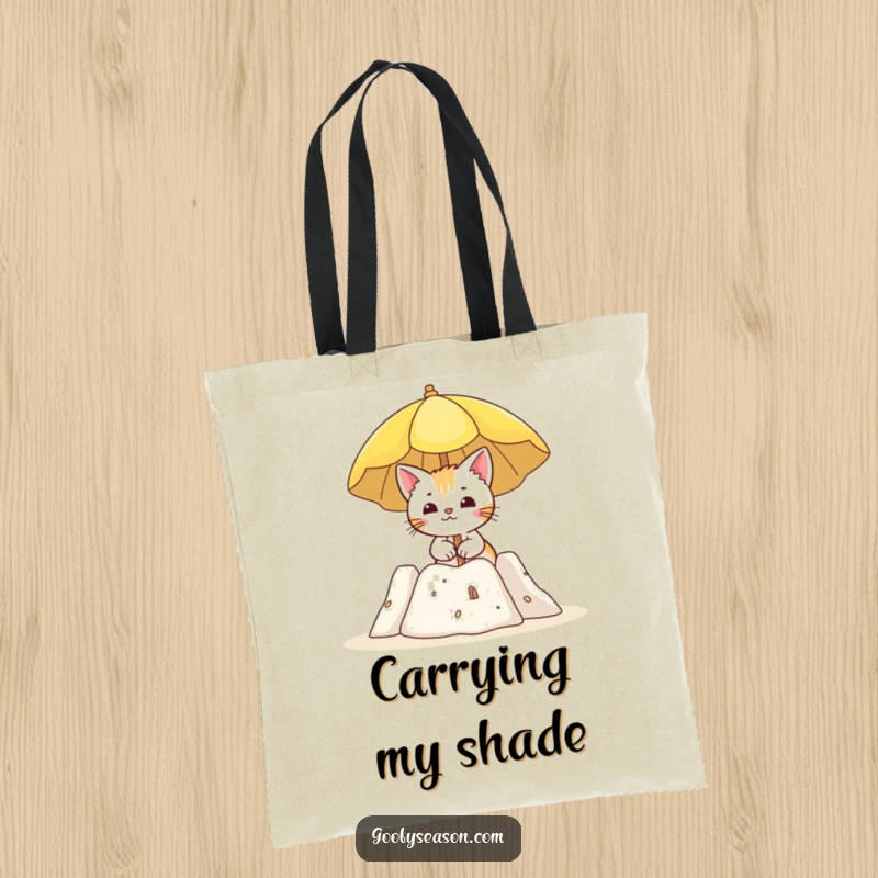 Funny tote bag featuring a curious cat holding a sun umbrella beside a sandcastle, ready for beach trips.