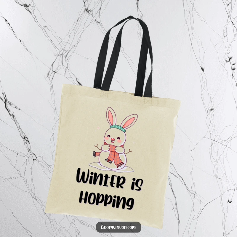 Funny tote bag featuring a happy bunny character decorating a snowman with a scarf, ready for winter adventures.